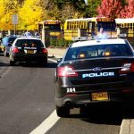 Police cars with lights on near school buses on a city street