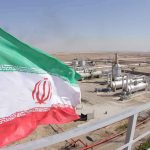 Iran’s Shadow RULER VANISHES — Who’s REALLY In Charge? Iran flag over an oil and gas facility in a desert landscape