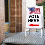 UNEXPECTED Poll TWIST Jolts DEEP-BLUE Narrative Sidewalk sign with American flag directing to a polling place
