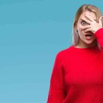 Woman in red sweater peeking through fingers with a surprised expression