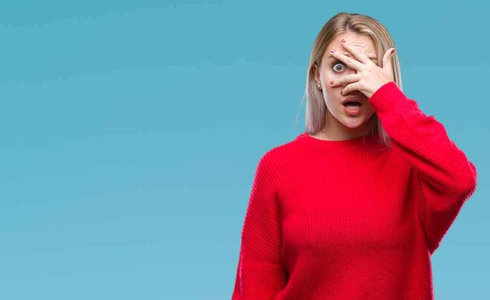Woman in red sweater peeking through fingers with a surprised expression