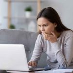 Old CONFESSION EXPLODES — Governor Race in JEOPARDY Woman on couch looking at laptop with hand over mouth