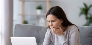 Woman on couch looking at laptop with hand over mouth