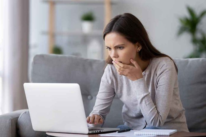 shutterstock_1297544869 Woman on couch looking at laptop with hand over mouth