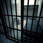 Interior view of a prison cell with a bed and metal bars