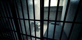 Interior view of a prison cell with a bed and metal bars