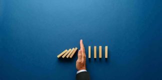 Hand stopping falling wooden dominoes on blue background