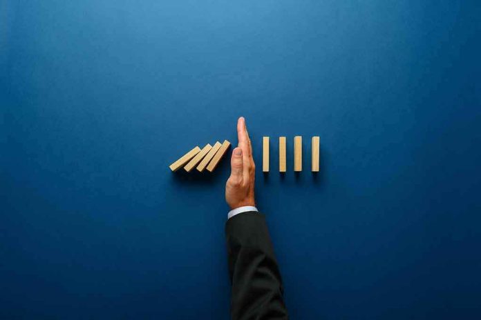 shutterstock_1509665324 Hand stopping falling wooden dominoes on blue background