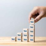 Pension TIME BOMB Triggers Costly TAX Hike Hand stacking wooden blocks labeled TAX into ascending columns