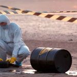 Nuclear Dump Deal ALARMS Residents — Rightly SO! Hazmat worker kneeling near a fallen barrel at a cordoned-off site