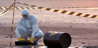 Nuclear Dump Deal ALARMS Residents — Rightly SO! Hazmat worker kneeling near a fallen barrel at a cordoned-off site