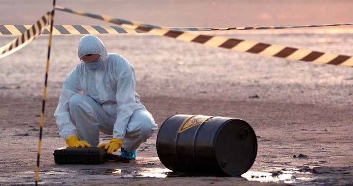 shutterstock_1776364469 Hazmat worker kneeling near a fallen barrel at a cordoned-off site