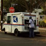 Mail carrier standing behind a USPS truck on a suburban street