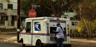 Mail carrier standing behind a USPS truck on a suburban street