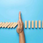 Judge Blocked It — ICE Did It Anyway! Hand stopping falling wooden dominoes on blue background