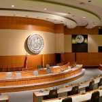 Justice Watchdog GUTTED — Who Stops Abuse NOW? Interior view of a government chamber with wooden paneling and seating