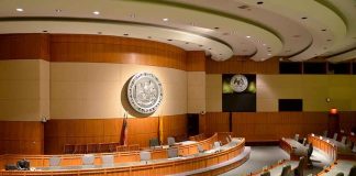 Justice Watchdog GUTTED — Who Stops Abuse NOW? Interior view of a government chamber with wooden paneling and seating
