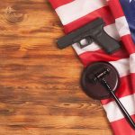 SHOCKING Question ANSWERED — Second Amendment TWIST Handgun and judge's gavel on American flag over wooden table