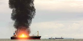 Cargo ship on fire with thick black smoke at sea