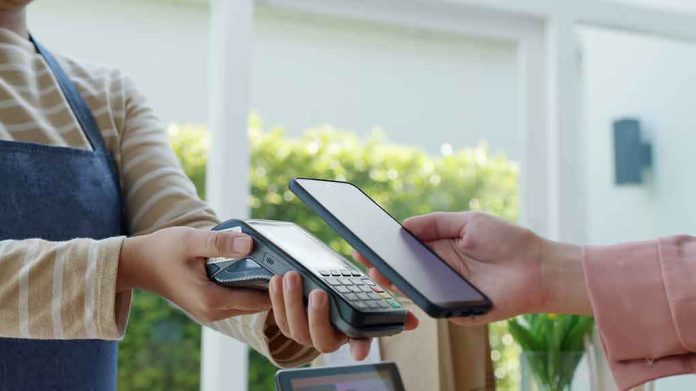 shutterstock_2059763165-1 Customer paying with smartphone at contactless card reader
