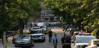 Police officers secure a residential street with patrol cars and yellow tape