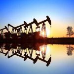 Oil pumpjacks at sunset reflected in still water