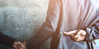 businessperson shakes hands while crossing fingers behind back