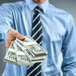 Person in business attire offering bundles of US dollar bills