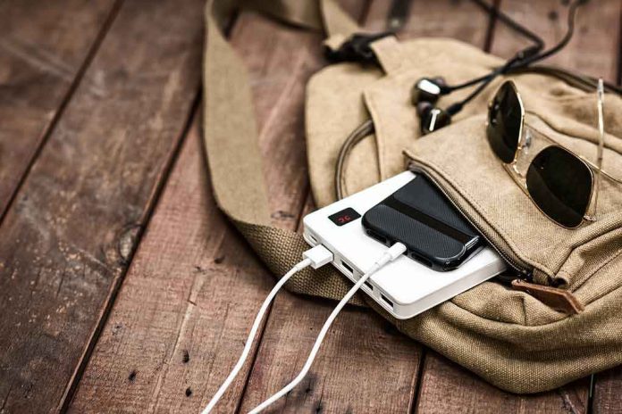 shutterstock_1043973061 Beige backpack with phone charging on power bank and sunglasses