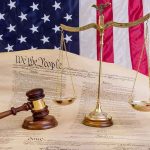 Scales of justice and gavel on the U.S. Constitution with American flag backdrop