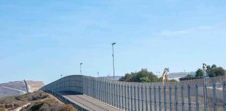 Tall metal border fence curving through arid landscape