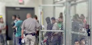 People standing inside chain-link holding area with an officer nearby
