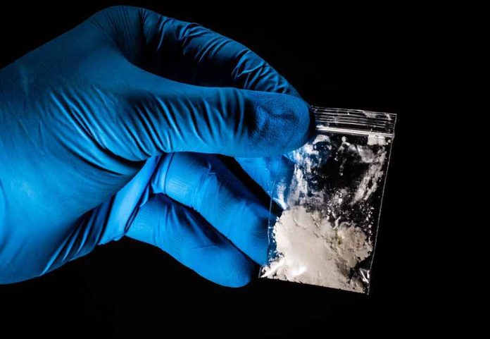 shutterstock_1272023845-1 Gloved hand holding a small plastic bag of white powder