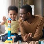 Trump UPENDS Child Care — What Changes Now? Child and adult building a tall tower with colorful wooden blocks