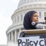 Omar’s Power Play Stuns Democrats Ilhan Omar speaking at a podium with microphones in front of the U.S. Capitol