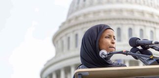 Ilhan Omar speaking at a podium with microphones in front of the U.S. Capitol