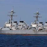 Three gray naval destroyers docked side by side at a pier