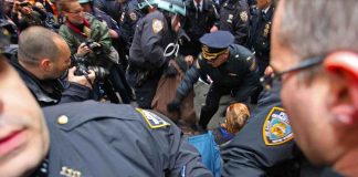 Police officers detain a person during a crowded street protest