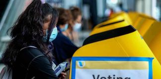 UNEXPECTED Power Shift Brewing In New Hampshire voter wearing a mask using a yellow ballot box