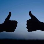 two hands giving thumbs up against a blue sky