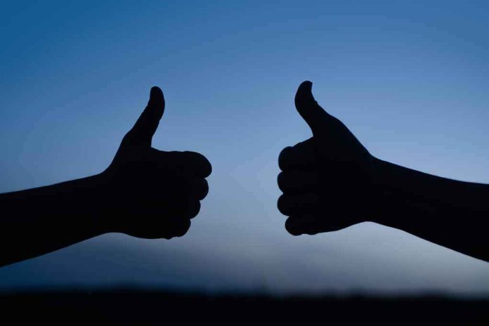 two hands giving thumbs up against a blue sky