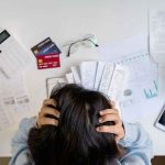 Check Your Next Card Statement — The Fed Just Made It WORSE Person holding head over bills and credit cards on desk