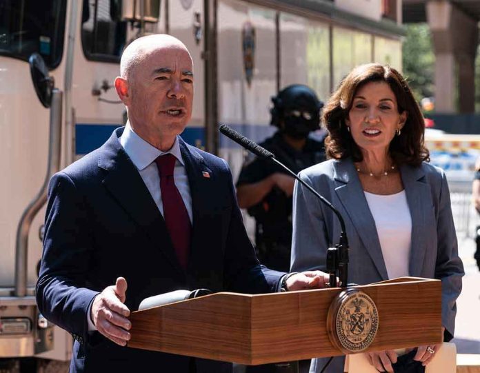 shutterstock_2040385199 Alejandro Mayorkas speaks at a podium with Kathy Hochul standing beside him outdoors