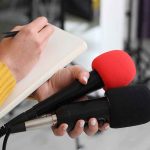 Sound Waves Zap Parkinson’s Tremor in Minutes! Journalist holding two microphones while writing in a notebook