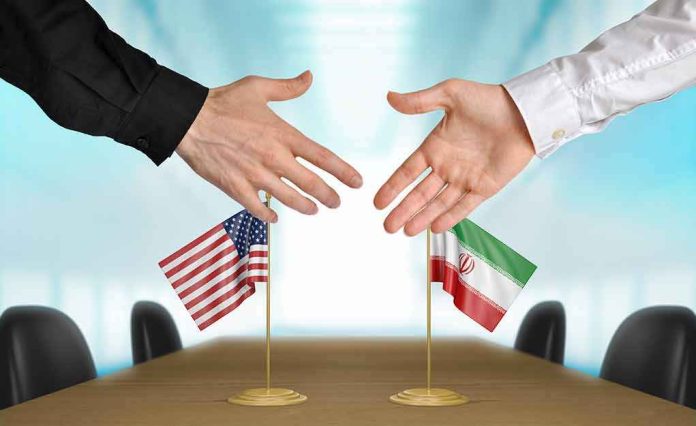 shutterstock_274494032-1 Two hands reaching to shake above US and Iran flags on a conference table
