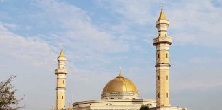 Mosque with golden dome and two tall minarets under a partly cloudy sky