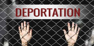 Hands gripping chain-link fence with deportation sign
