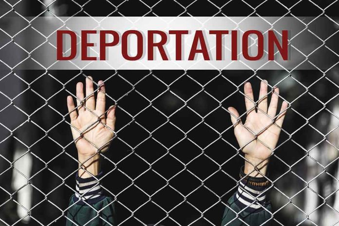 shutterstock_519187753 Hands gripping chain-link fence with deportation sign