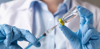 Gloved hands drawing liquid from a vial with a syringe