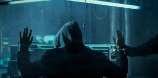 Hooded person at computer raises hands as another clamps handcuffs